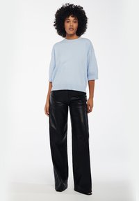 Lichtblauwe gebreide trui met korte, verlaagde mouwen, gecombineerd met zwart kunstleren hoge taille wijde broek. Gladde textuur en losse pasvorm.