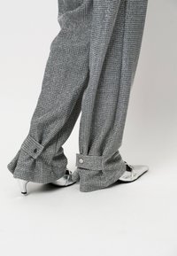 Grijs gestreepte broek met een losse pasvorm, voorzien van knoopdetails bij de zoom; gecombineerd met puntige zilveren hoge hakken. Gladde stofstructuur.