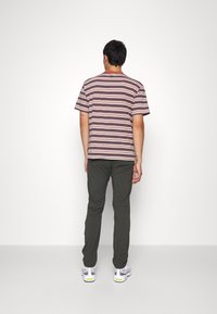 Kortärmad randig t-shirt i jordnära färger, matchad med olivgröna byxor. T-shirten har breda horisontella ränder och en avslappnad passform.