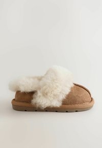 Ruskean suede-tossut, joissa on pörröinen valkoinen shearling-reuna. Pehmeä materiaali, pyöreä muoto ja litteä, teksturoitu pohja.