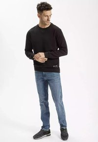 Czarna bluza z ribbowymi mankietami i hemem, zestawiona z jasnoniebieskimi dżinsami i czarnymi trampkami. Minimalistyczny design, bez wzorów i grafik.