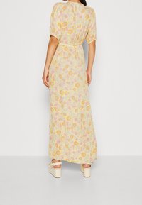 Maxikjole i let, svævende stof med en gul bund, prydet med pink og orange blomster mønstre, korte puffærmer og en sammenpresset talje.