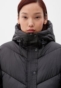 Czarna puchowa kurtka z wysokim kołnierzem, z pikowaną teksturą, detalami z wyciąganą sznurkiem oraz wieloma guzikami na przednim zapięciu.