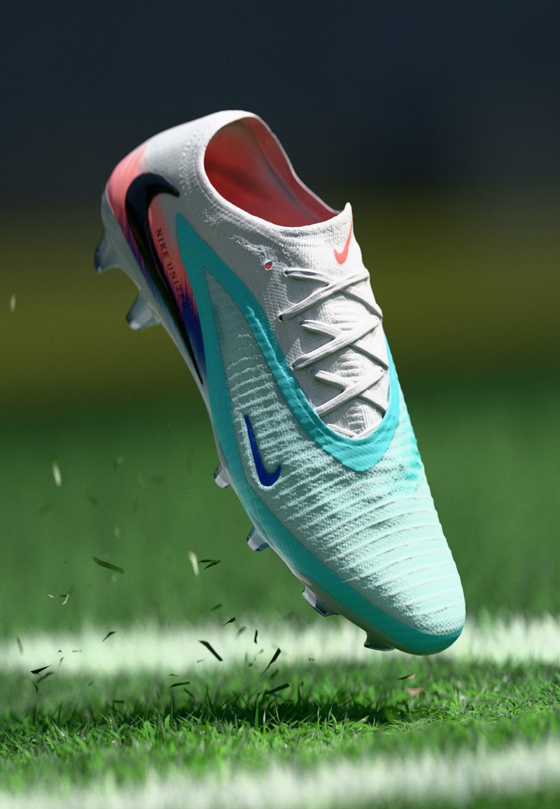 Nike soccer cleat in white with teal and pink accents, featuring a textured upper, rounded toe, and multi-directional studs for traction.