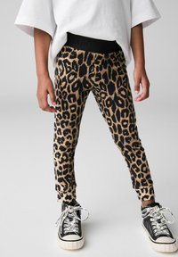 Legginsy w panterkę w odcieniach beżu i czerni z czarnym elastycznym paskiem z napisem 'SAINTS'; w połączeniu z czarnymi sneakersami i wzorzystymi sznurowadłami.