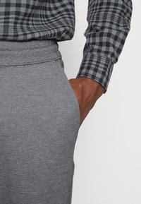 Pantalones deportivos grises con una tela texturizada, con un corte relajado y una cintura elástica, combinados con una camisa de manga larga a cuadros en negro y gris.