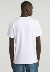 Camiseta de algodón blanca con mangas cortas y un cuello redondo clásico, con una textura suave y un ajuste relajado, vista desde la parte de atrás.