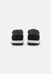 Czarne zamszowe i białe skórzane sneakersy mają niski profil, wyściełany kołnierz oraz teksturowaną gumową podeszwę z logo na pięcie.