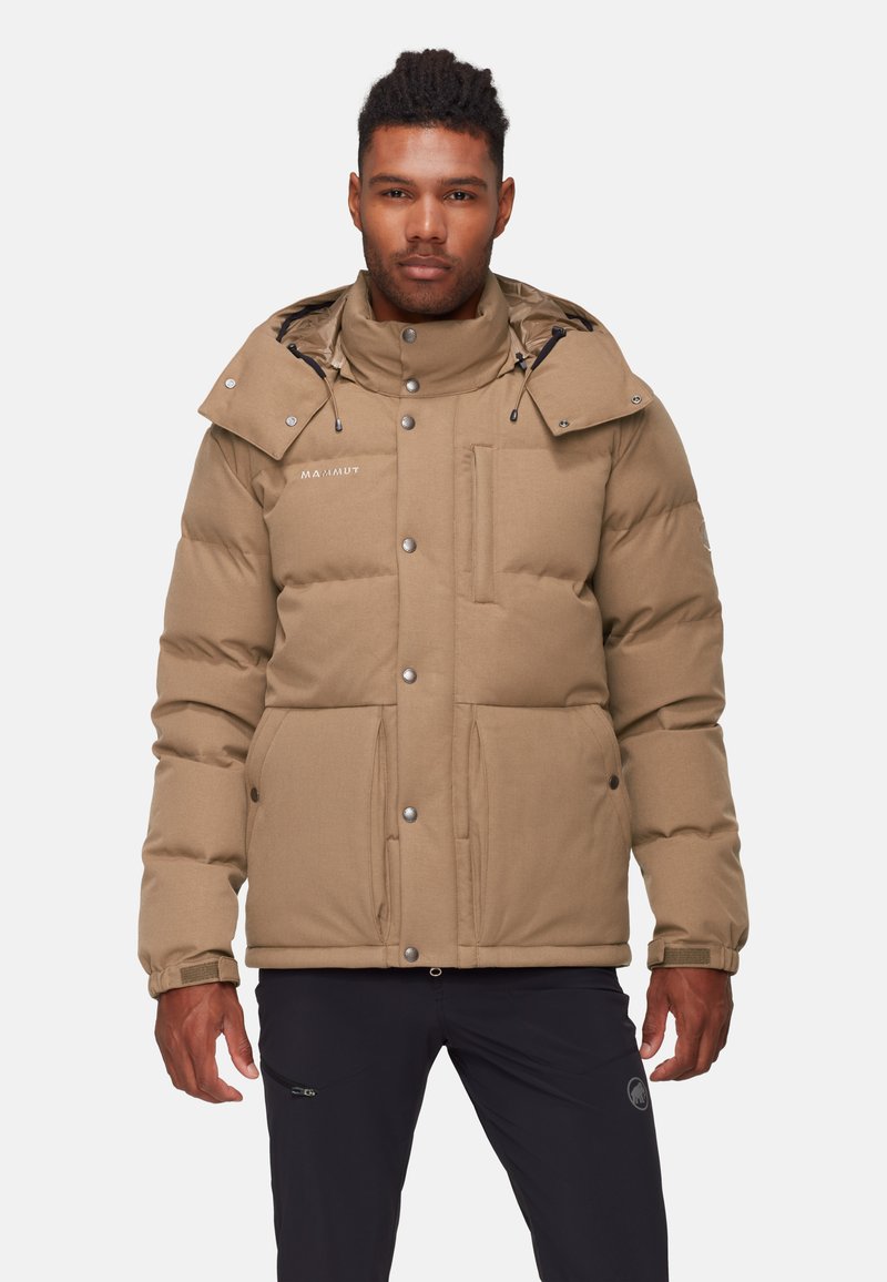 Giacca puffer color cammello con colletto alto, cappuccio regolabile, tasche frontali con zip e polsini a coste. Presenta un dettaglio con logo sul petto.