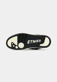 Μαύρη και άσπρη σόλα παπουτσιού Etnies με υφή από καουτσούκ, ζιγκ-ζαγκ σχέδιο, κυκλικά στοιχεία και σήμανση με έντονους χαρακτήρες.