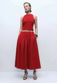 Top corto rosso abbinato a una gonna plissettata alta in vita rossa. L'outfit presenta una texture liscia e un design minimalista. Sandali neri con cinturini.