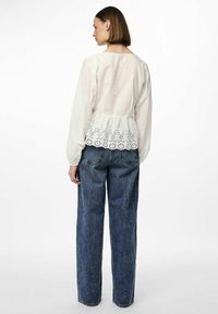Blusa bianca a maniche lunghe con vita arricciata e dettaglio in pizzo ad occhio all'orlo, abbinata a jeans denim blu larghi.