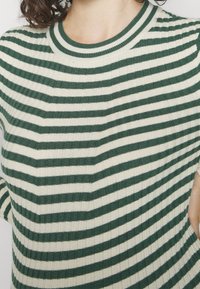 Maglione a righe verde e crema con texture a coste e scollo rotondo, dotato di maniche corte e un design complessivamente aderente.