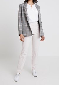 Gray plaid blazer with light pink lines, black buttons; paired with a white henley shirt and light beige trousers, finished with white sneakers.