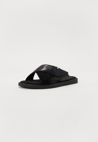 Sorte sandaler i svart med kryssremdesign laget av glatt skinn og mykt semsket skinn. Flat såle med en teksturert fotseng for godt grep.