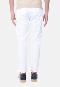 Pantaloni di cotone bianchi con una vestibilità slim, dotati di tasche posteriori, abbinati a scarpe nere e un delicato dettaglio in pizzo alla caviglia.