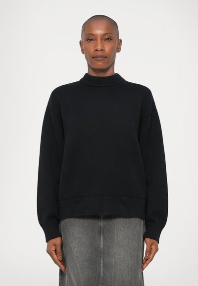 Pull en tricot noir avec un col montant, coupe décontractée et ourlet côtelé. Tissu texturé et manches longues assortis à une jupe grise.