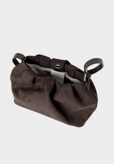 Borsa a mano in suede marrone con una forma morbida e raccolta, doppi manici in pelle e un interno chiaro in contrasto. Presenta una chiusura con gancio metallico.