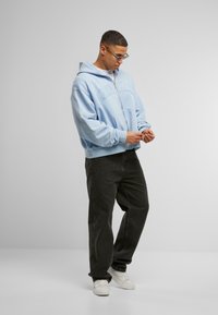 Lyseblå hættebluse med frontlomme og præget tekst, parret med sorte lige ben jeans og hvide sneakers.