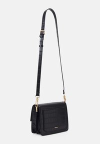 Borsa a tracolla in pelle nera con texture, cinturino regolabile e hardware dorato, forma rettangolare con pattina frontale e logo discreto.