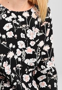 Černá látka s květinovým vzorem, která obsahuje bílé a pastelově růžové květy a zelené stonky. Kulatý výstřih a jemná textura.