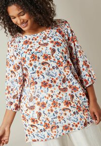 Bluse med blomstermønster på hvid baggrund, med orange, blå og røde blomster. Løs pasform, trekvartærmer, struktureret stof.