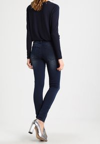 Skinny dark blue denim jeans with back pockets, paired with metallic silver high-heeled shoes and a long-sleeve navy top.