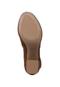 Semelle de chaussure en daim marron avec un grip en caoutchouc texturé sur l'avant et l'arrière, vue du dessous sur fond blanc.