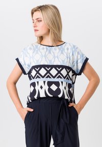 Patterned blouse with short sleeves; features light blue, navy, and white geometric designs; soft fabric with a relaxed fit.