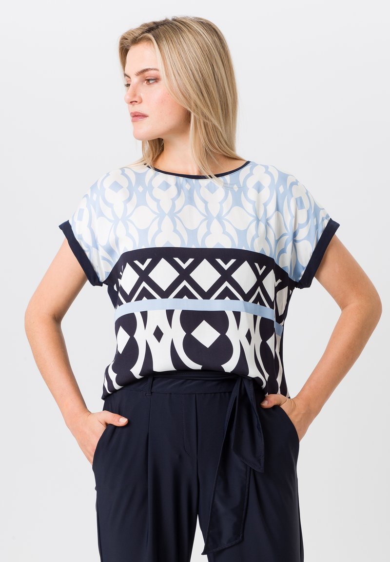 Patterned blouse with short sleeves; features light blue, navy, and white geometric designs; soft fabric with a relaxed fit.