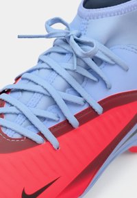 Scarpa sportiva blu con dettagli rossi, dotata di un materiale superiore liscio, lacci intricati e una suola testurizzata per una migliore trazione.
