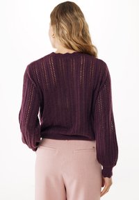 Maglione in pizzo color prugna con texture a costine e maniche a palloncino, abbinato a pantaloni su misura rosa chiaro. La vista posteriore mette in evidenza il design dettagliato.