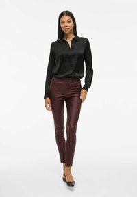 Camicia in satin nera con bottoni e maniche lunghe, abbinata a pantaloni slim fit bordeaux e ballerine nere a punta, su un modello davanti a uno sfondo bianco.