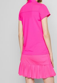 Malinově růžové sportovní šaty se přiléhavým vrškem a rozšířenou sukní, s texturovaným horním dílem, sklady na okraji a tečkovaným vzorem na sukni.