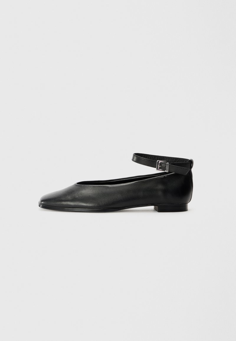 Ballerine in pelle nera con punta affusolata e sottile cinturino alla caviglia, caratterizzate da un tacco basso e una trama liscia. Design semplice e minimale.