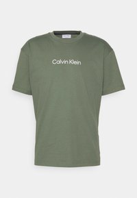 Oliwkowa bawełniana koszulka z krótkim rękawem i okrągłym dekoltem; na przedzie znajduje się biały nadruk z logo "Calvin Klein".