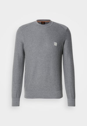 Szürke, kötött pulóver hosszú ujjakkal, bordás mandzsettákkal és kerek nyakkivágással. A mellrészen egy kis négyzet alakú logó található.