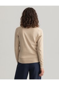 Beige trui met geribbelde mouwen en onderrand, gemaakt van zacht materiaal. Kenmerkt zich door een klassieke snit met aangebrachte mouwen en een gladde textuur.