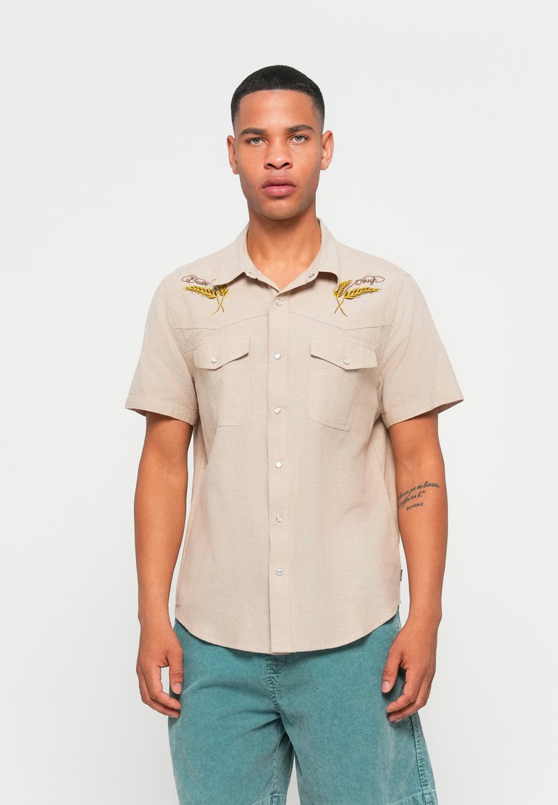 Short-sleeve beige shirt with two chest pockets, featuring yellow embroidered wheat designs on the shoulders and button-up front.