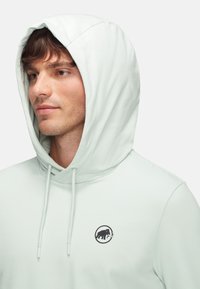 Helle mintgrüne Kapuzenjacke aus weichem Material, mit Kordelzugkapuze und einem schwarzen kreisförmigen Logo mit einem Elefanten. Glatte Textur und lässige Passform.