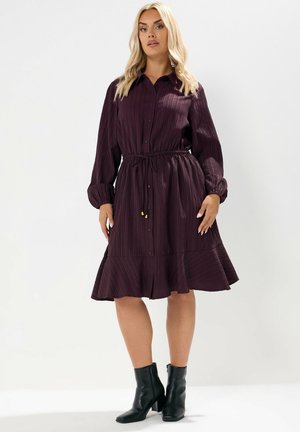 Dunkellilahe Hemdkleid mit vertikalem Rippstruktur, langen Ärmeln, Knopfverschluss und geraffter Taille. Es hat einen ausgestellten Saum und wird mit schwarzen Stiefeletten kombiniert.