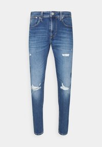 Modré skinny džíny vyrobené z denimu, s bledým praním, s vyraženými záplatami na přední straně a klasickým designem s pěti kapsami.