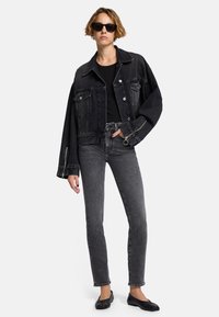 Zwarte denimjas met een losse pasvorm, grote zakken en zilverkleurige hardware; gecombineerd met strakke zwarte jeans en zwarte platte schoenen.