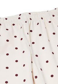 Tela de color crema con lunares marrones, con una cintura elástica. Textura suave con estampados circulares uniformemente distribuidos.