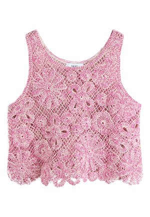 Femme en tenue crochet florale rose, lunettes de soleil jaunes et tongs, debout sous un parasol en bois dans un café en plein air avec des arbres et des chaises.