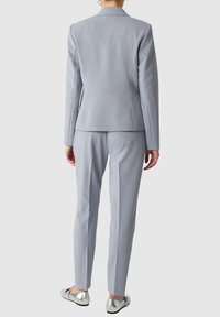 Completo grigio chiaro su misura con giacca strutturata e pantaloni slim-fit, realizzato in un tessuto morbido; abbinato a ballerine metalliche.