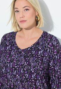 Top nero con un motivo astratto viola. Presenta un design a scollo a V e maniche corte. Tessuto liscio con una vestibilità comoda. Orecchini a cerchio dorati.