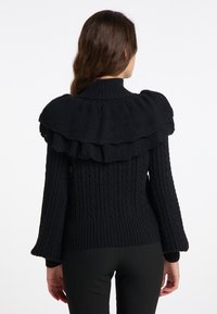Schwarzer gestrickter Pullover mit hohem Kragen und schichtigen Rüschendetails an den Schultern. Verfügt über eine gerippte Textur und Glockenärmel.