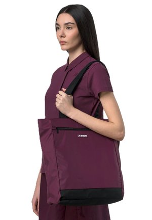 Donna con camicia color bordeaux che tiene una grande borsa bordeaux e nera con tasca frontale con cerniera sulla spalla.