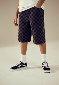 Sort og gråternet shorts med en afslappet pasform, parret med sorte sneakers og hvide ribbede sokker, der viser enkle designelementer.